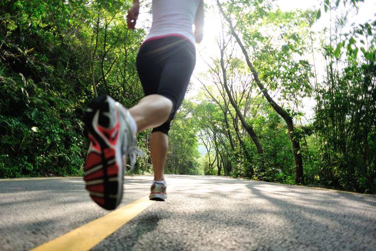 a woman running down a narrow road in the forest